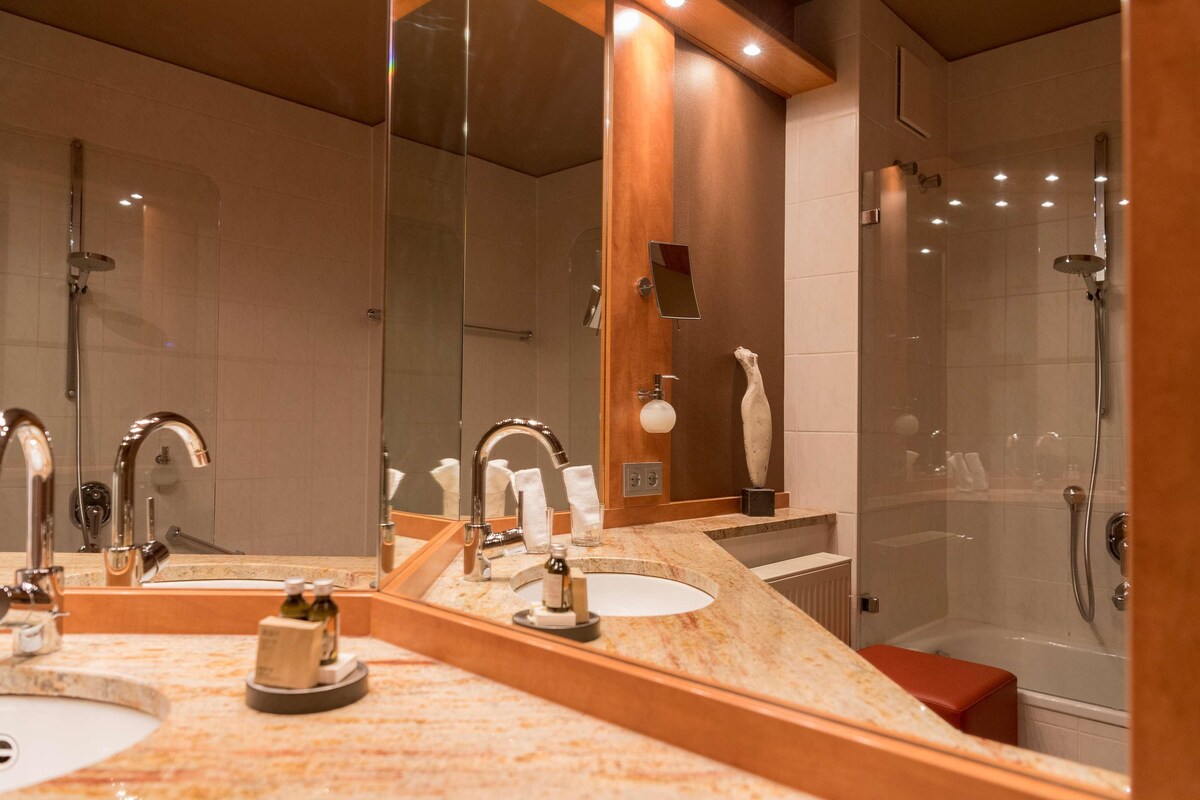 Un baño moderno con dos lavamanos, un espejo grande y una zona de ducha con mampara de cristal.
