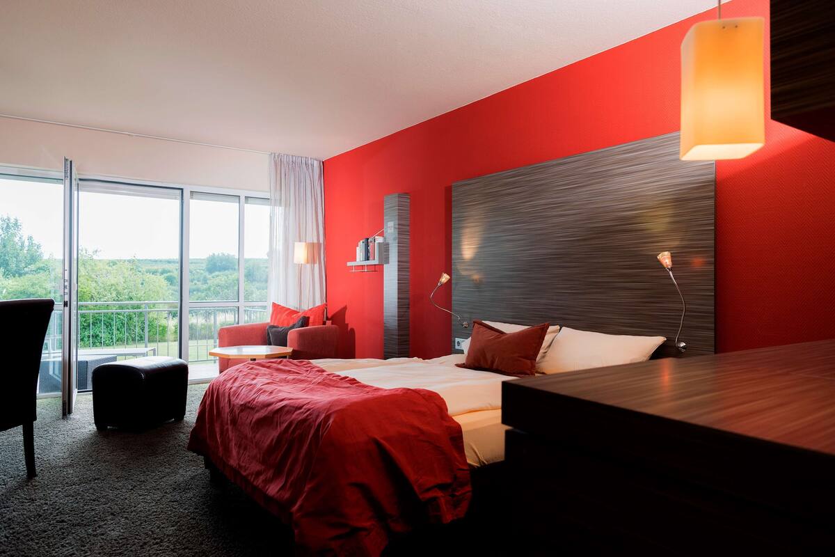 Ett modernt hotellrum med en stor säng, ett skrivbord, en stol och utsikt över omgivningarna.