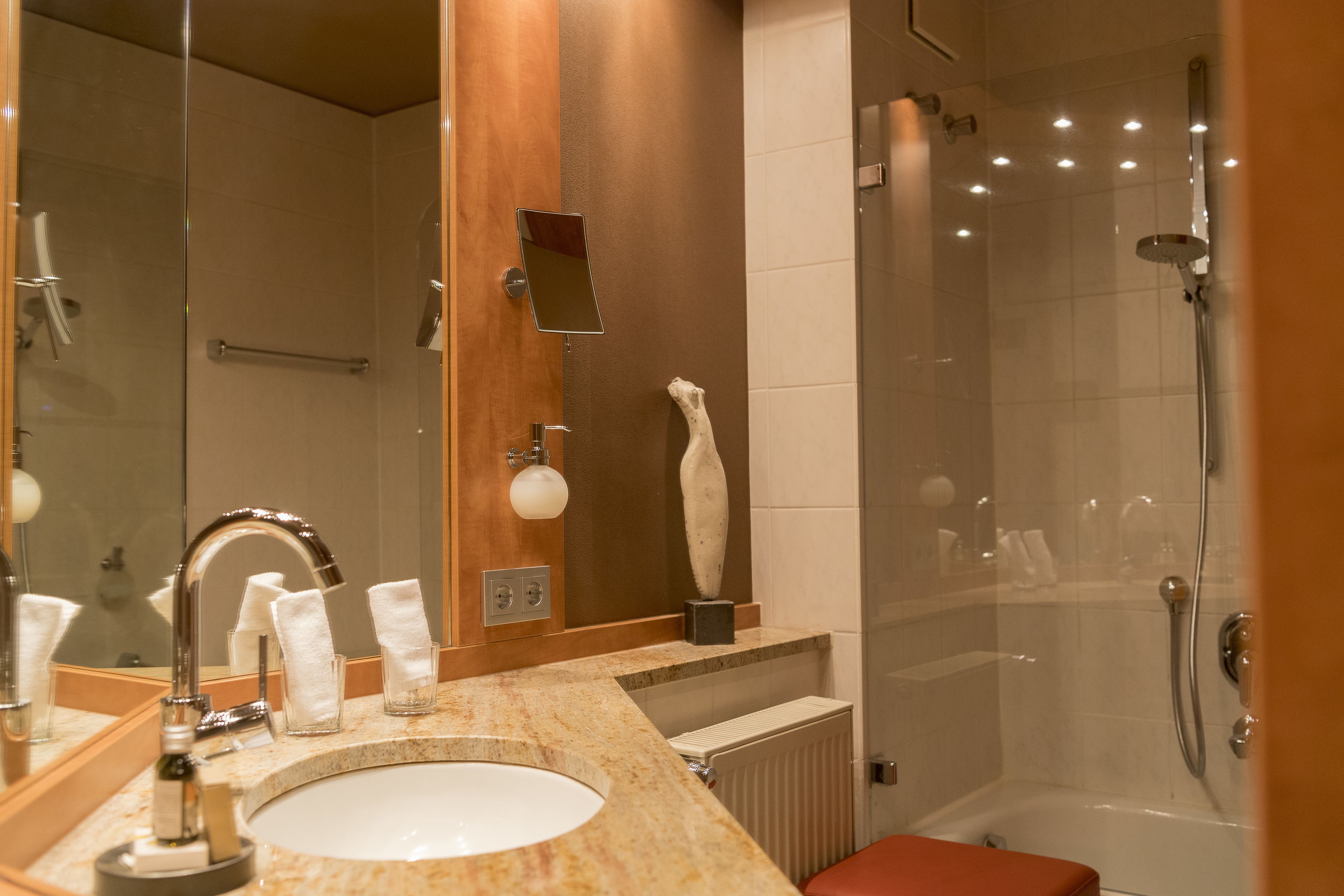 Ein modernes Badezimmer mit Waschbecken, Spiegel, Handtuchhalter und Duschbereich.