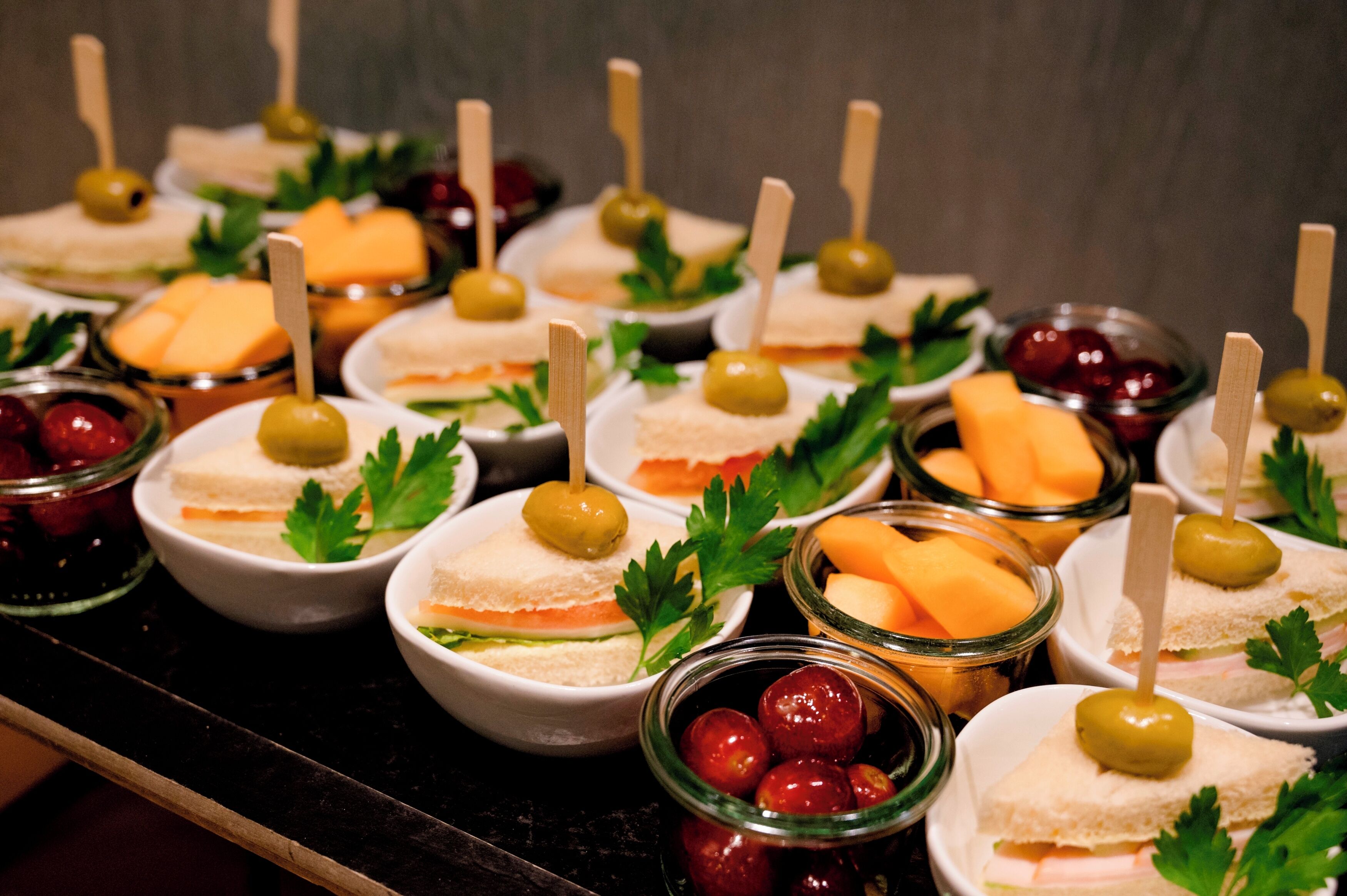 Een buffet met diverse soorten eten, waaronder belegde broodjes, olijven en fruit.