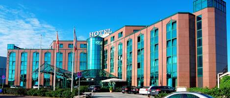 A modern hotel with a prominent "HOTEL" sign, a glass entrance, and a parking lot with several cars.