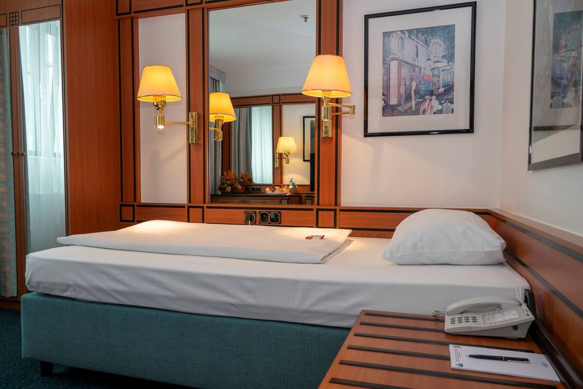 A hotel room with a bed, bedside lamps, a telephone, a framed picture, and a mirror.