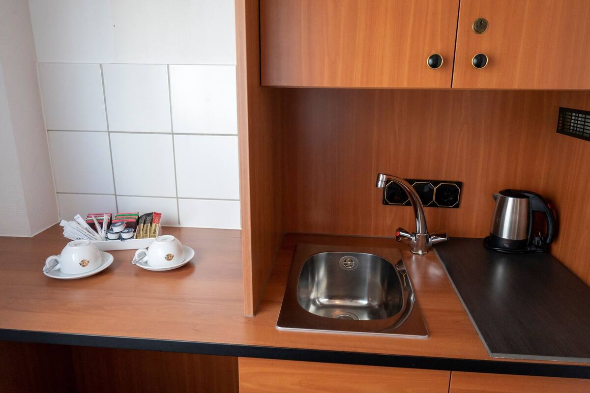 A modern kitchen with a stainless steel sink, a kettle, and a coffee maker. There are two white cups on the counter.