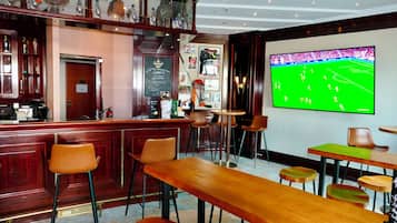 Zona de bar con muebles de madera, un televisor mostrando un partido deportivo y varias botellas en estantes.