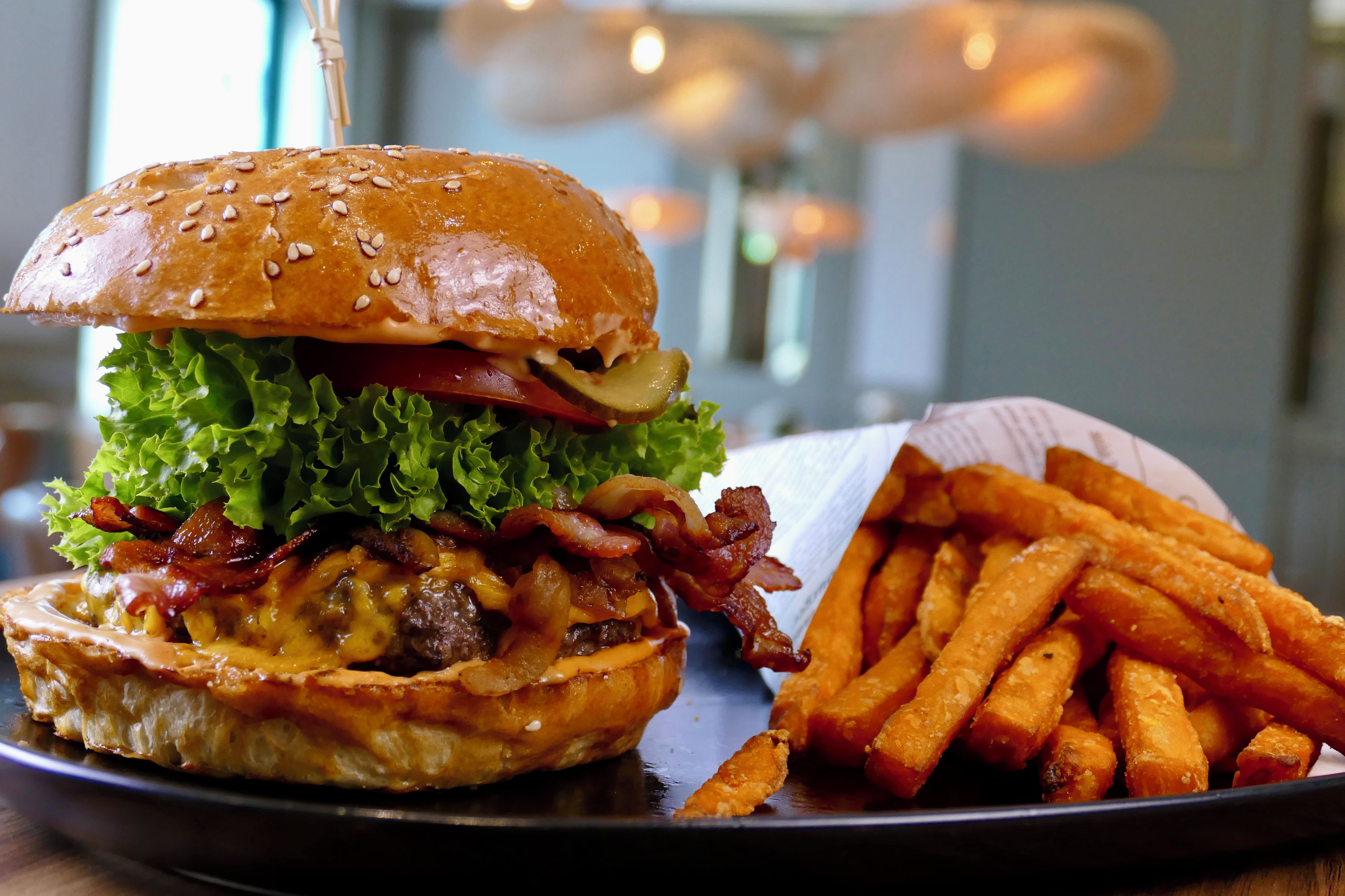 Una hamburguesa con lechuga, tocino y pan, junto a una cesta de papas fritas.