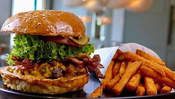 Una hamburguesa con lechuga, tocino y pan, junto a una cesta de papas fritas.