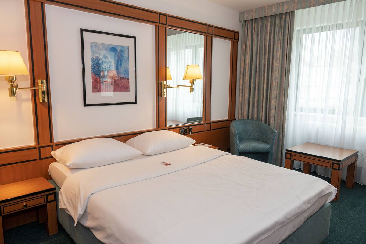 A hotel room with a large bed, a chair, a small table, and a painting on the wall.