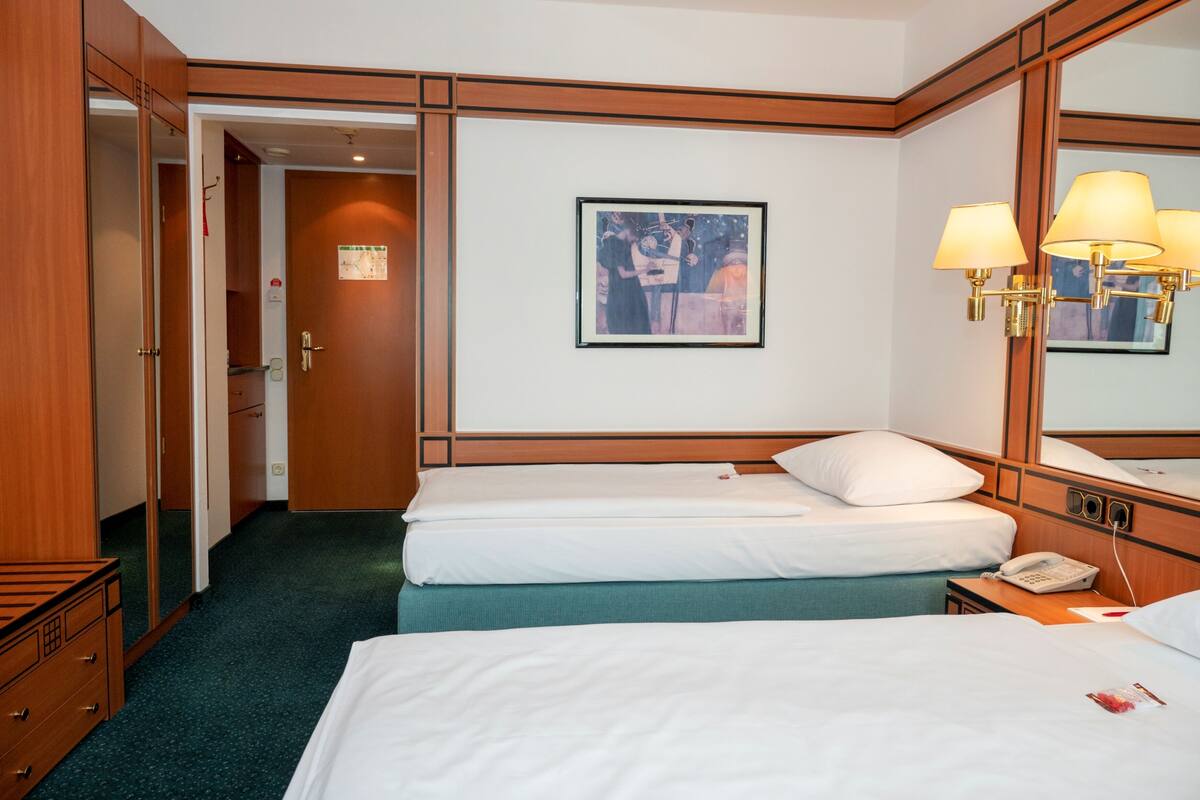 A hotel room with two beds, a large mirror, a framed picture on the wall, and a bedside table with a lamp.
