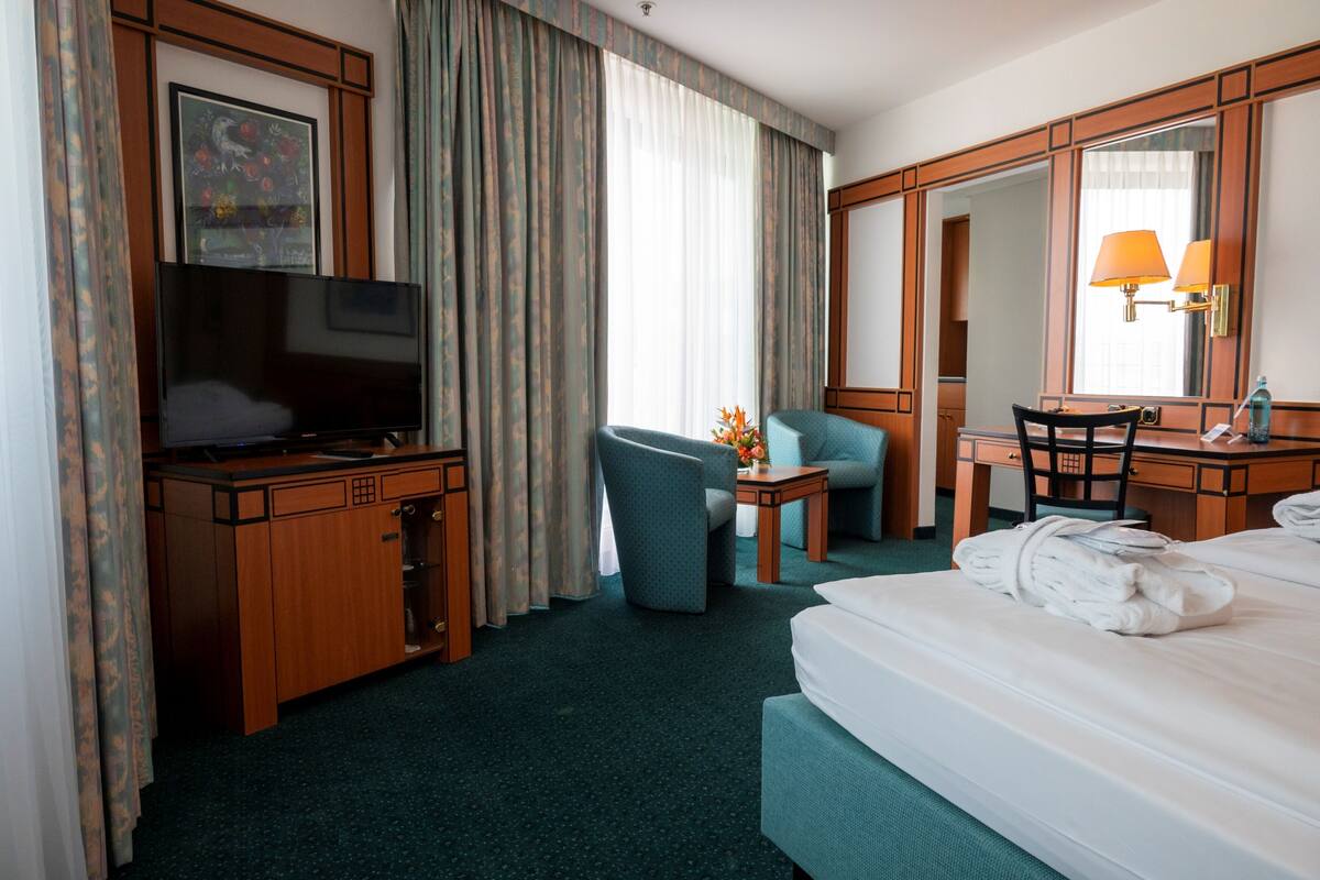 A hotel room with a bed, a desk with a television, a chair, a desk lamp, and a large mirror.