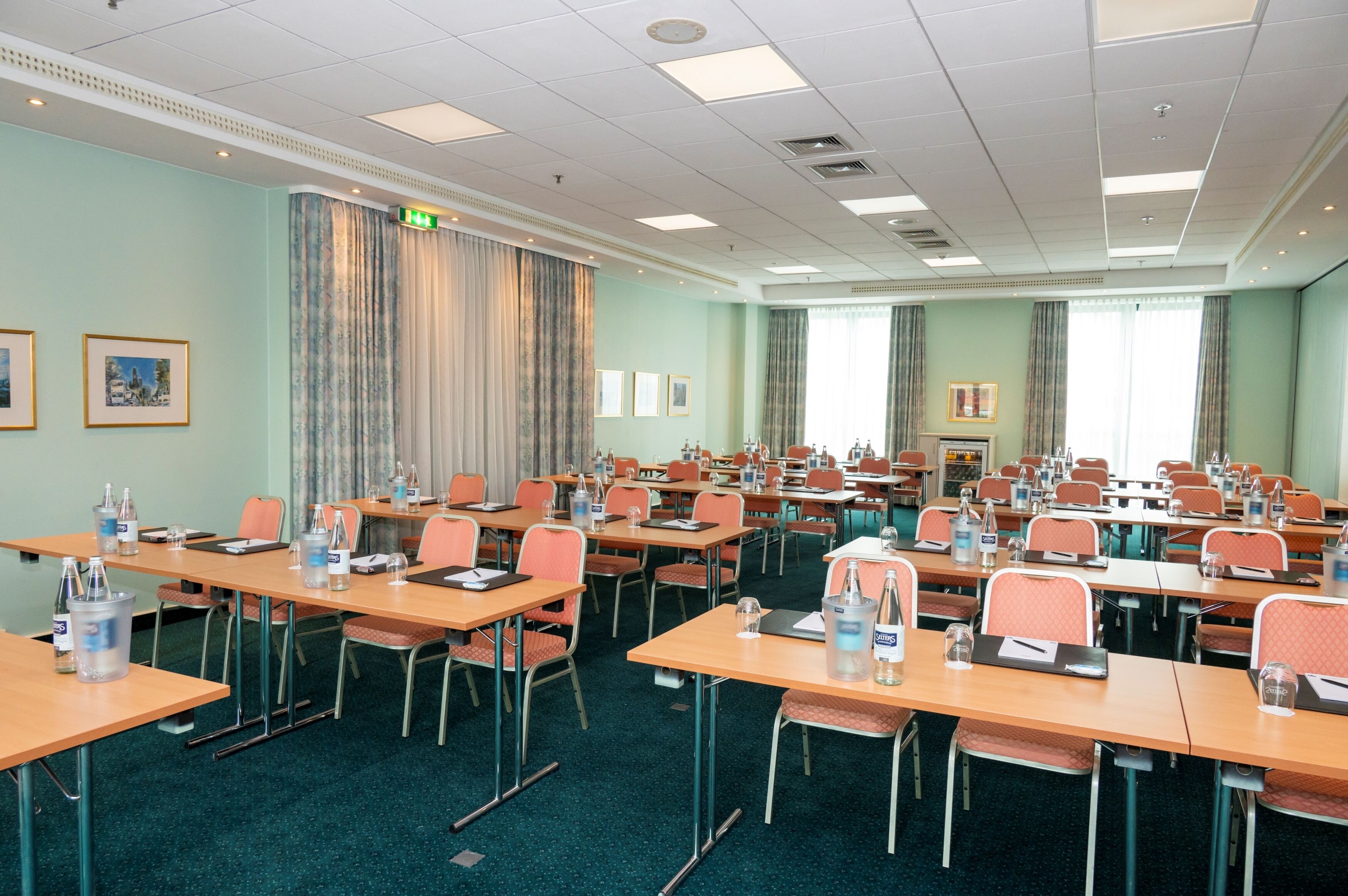 A conference room with multiple tables and chairs, equipped with water bottles and laptops.