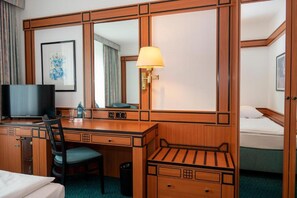 A hotel room with a wooden desk, a chair, a television, a bed, a bedside table, and a lamp. - Hotel Amadeus Frankfurt (Frankfurt)