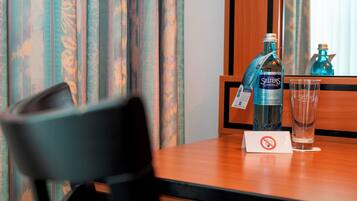 A hotel room with a wooden table, a bottle of Seiler's medium water, a glass, and a no-smoking sign.