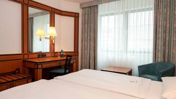 Ett hotellrum med en stor säng, ett skrivbord med två lampor, en stol och ett litet bord.