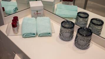 A bathroom vanity with a mirror, two folded towels, a box labeled 'Welcome', and several cylindrical containers.