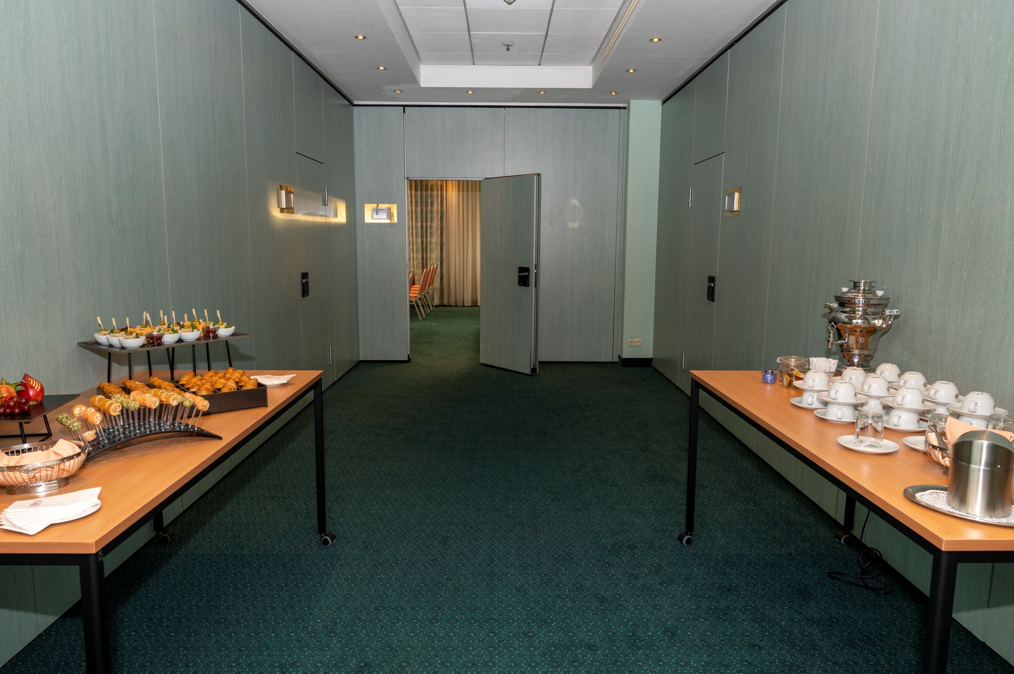 Un salón de conferencias con una larga mesa dispuesta para un bufé, una puerta que da a otra habitación y suelo alfombrado.