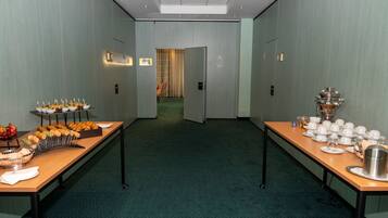 Un salón de conferencias con una larga mesa dispuesta para un bufé, una puerta que da a otra habitación y suelo alfombrado.