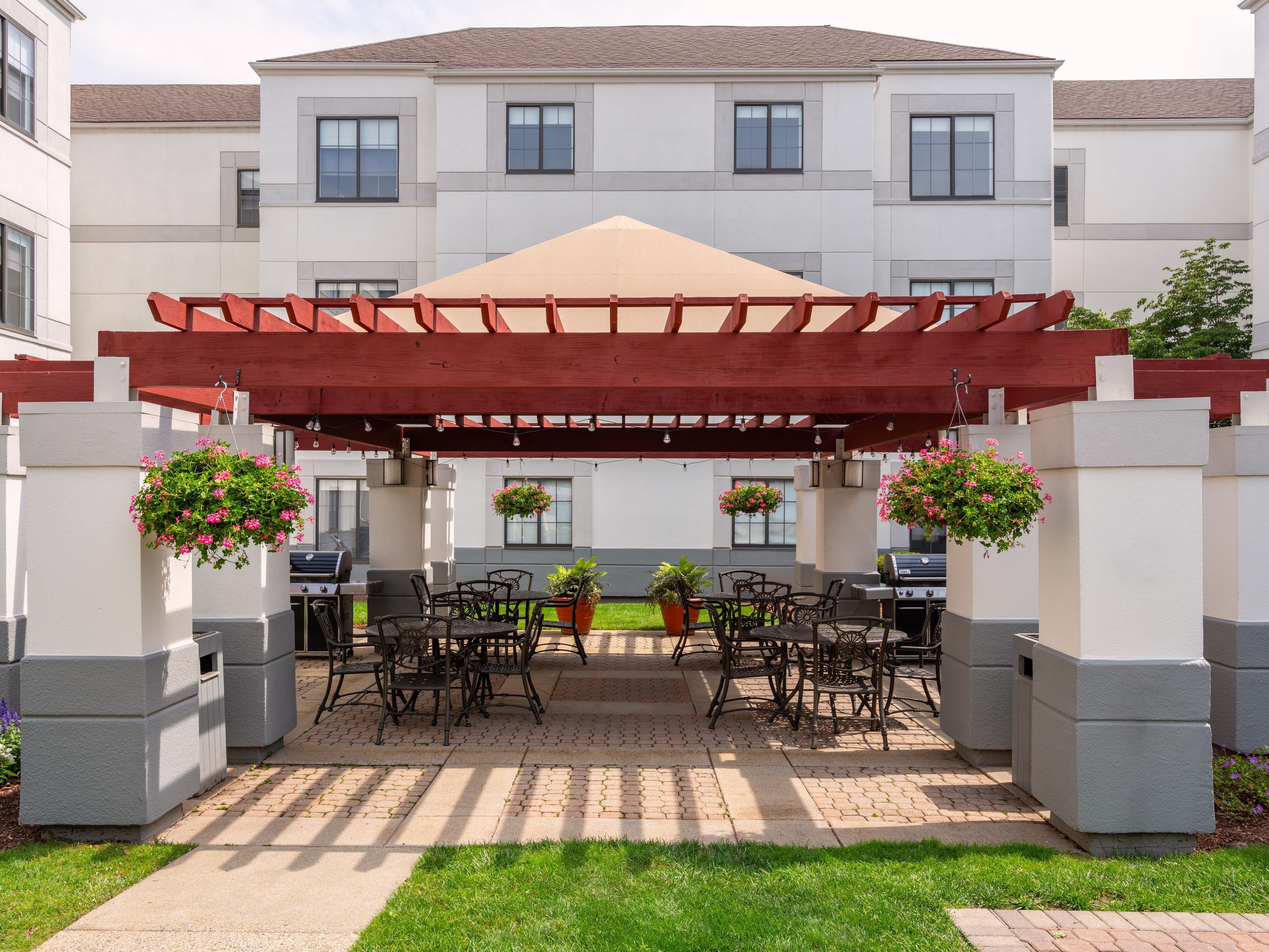 Un patio techado al aire libre con una pérgola, asientos exteriores y cestas de flores colgantes.