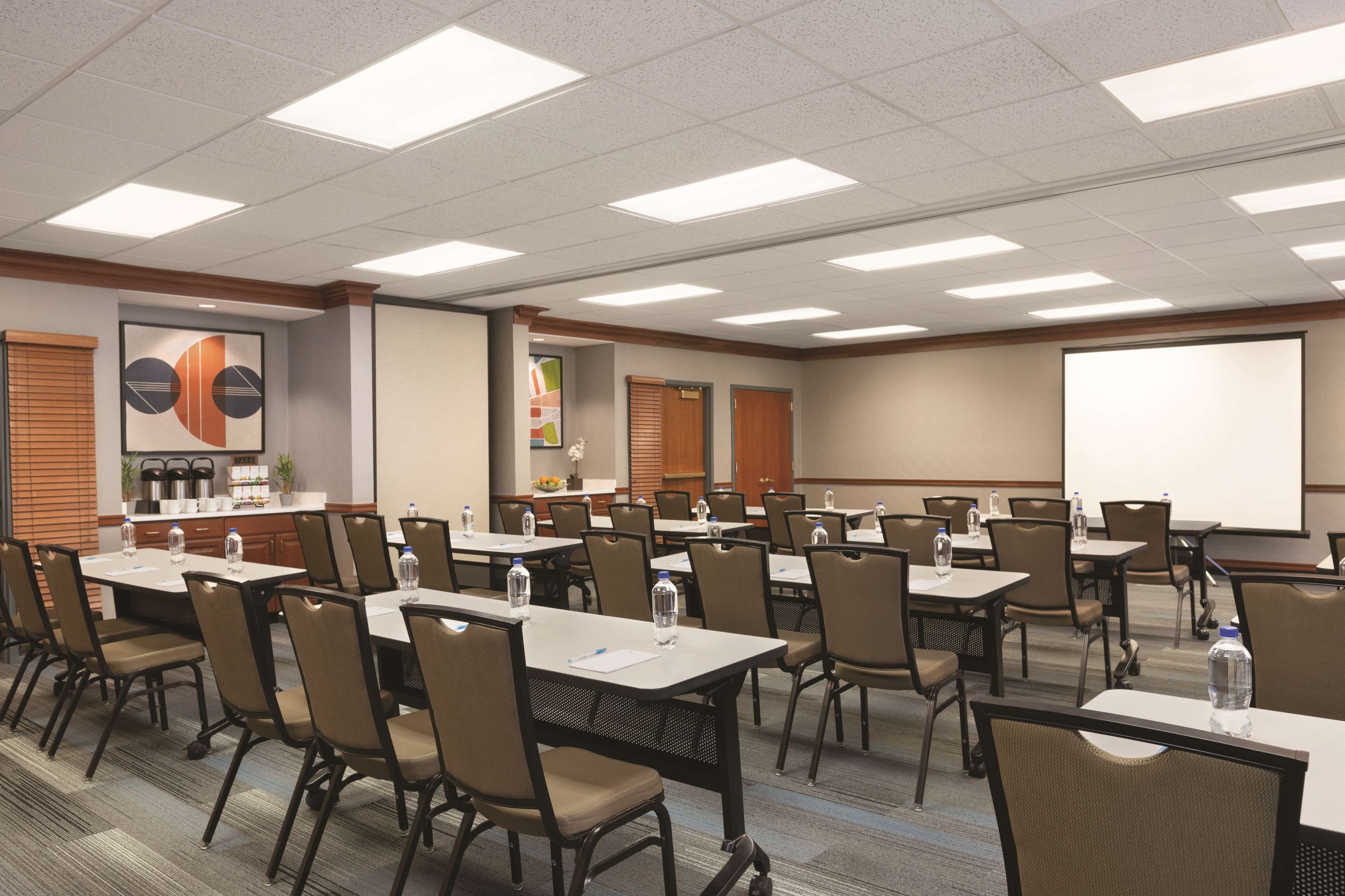 A conference room with multiple tables and chairs, equipped with water bottles and a projector screen.