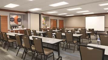A conference room with multiple tables and chairs, equipped with water bottles and a projector screen.