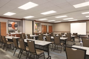 Una sala de conferencias con varias mesas y sillas, equipada con botellas de agua y una pantalla de proyector.