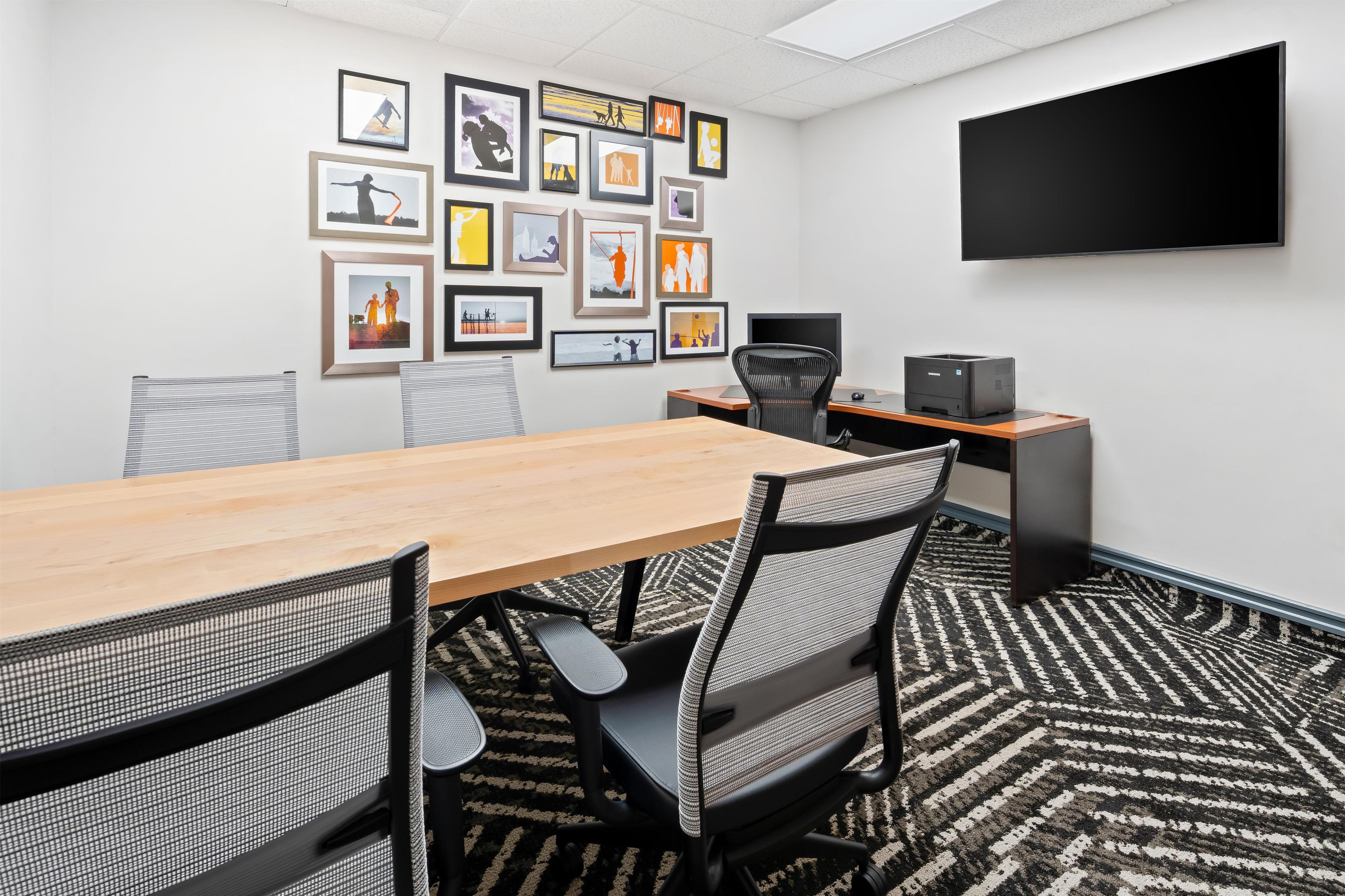 A conference room with a long table, chairs, a flat-screen TV, and framed pictures on the wall.