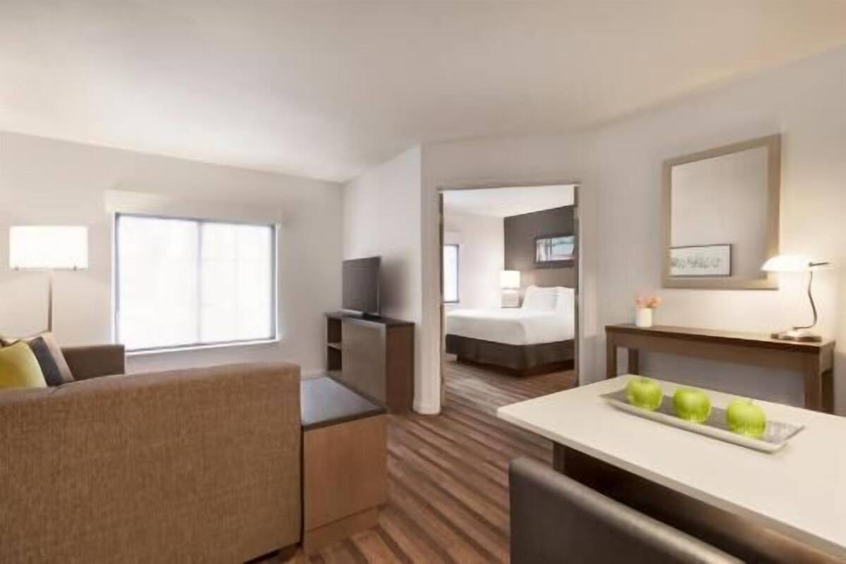 A hotel room with a sofa, a desk with a tray of apples, a TV, a bed, and a mirror.
