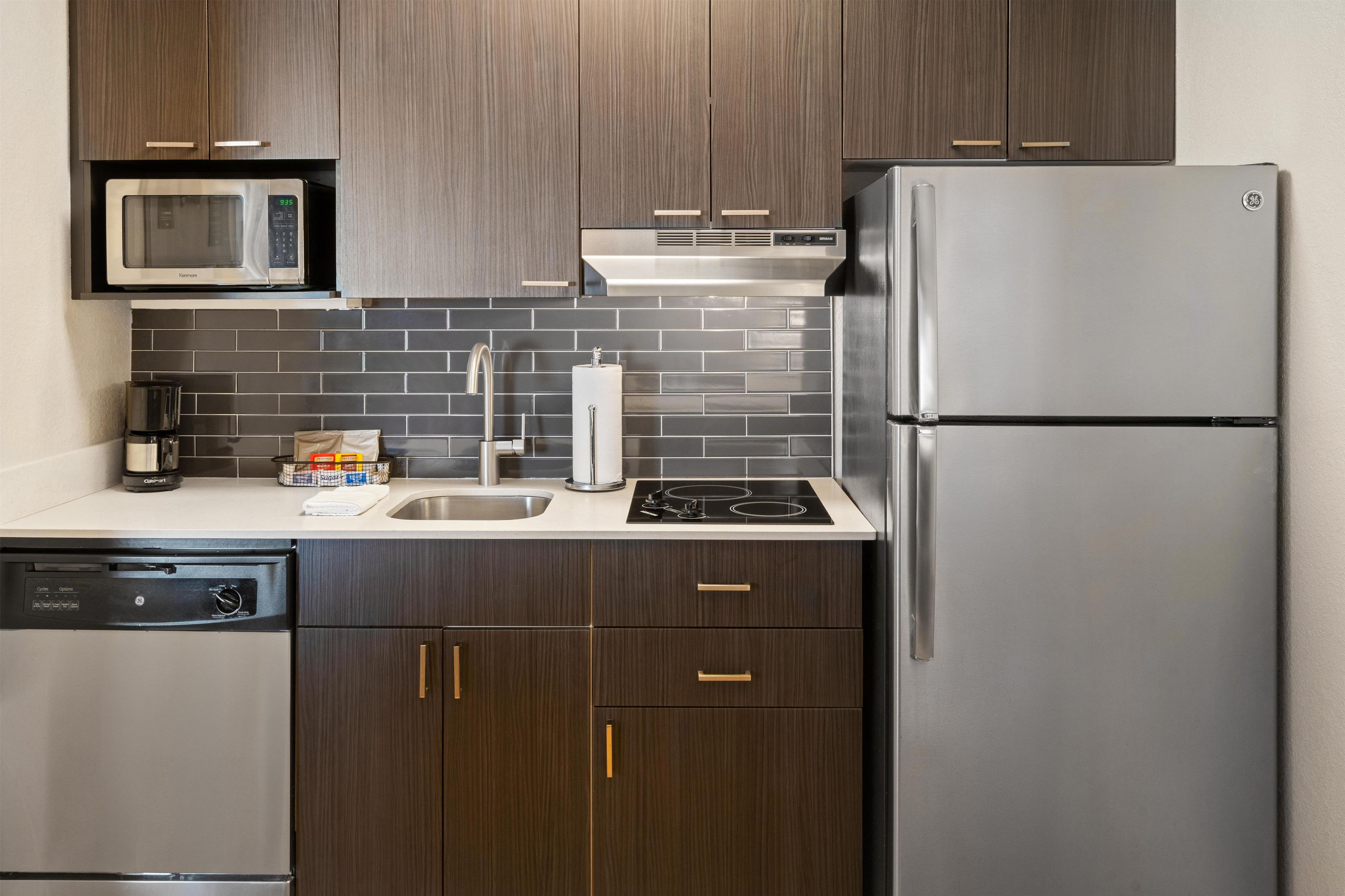 Een moderne keuken met donkerhouten kastjes, roestvrijstalen apparatuur en een betegelde spatwand.