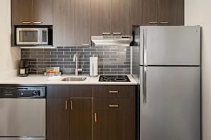 A modern kitchen with dark wood cabinets, stainless steel appliances, and a tiled backsplash. - HYATT house Boston/Burlington (Burlington)