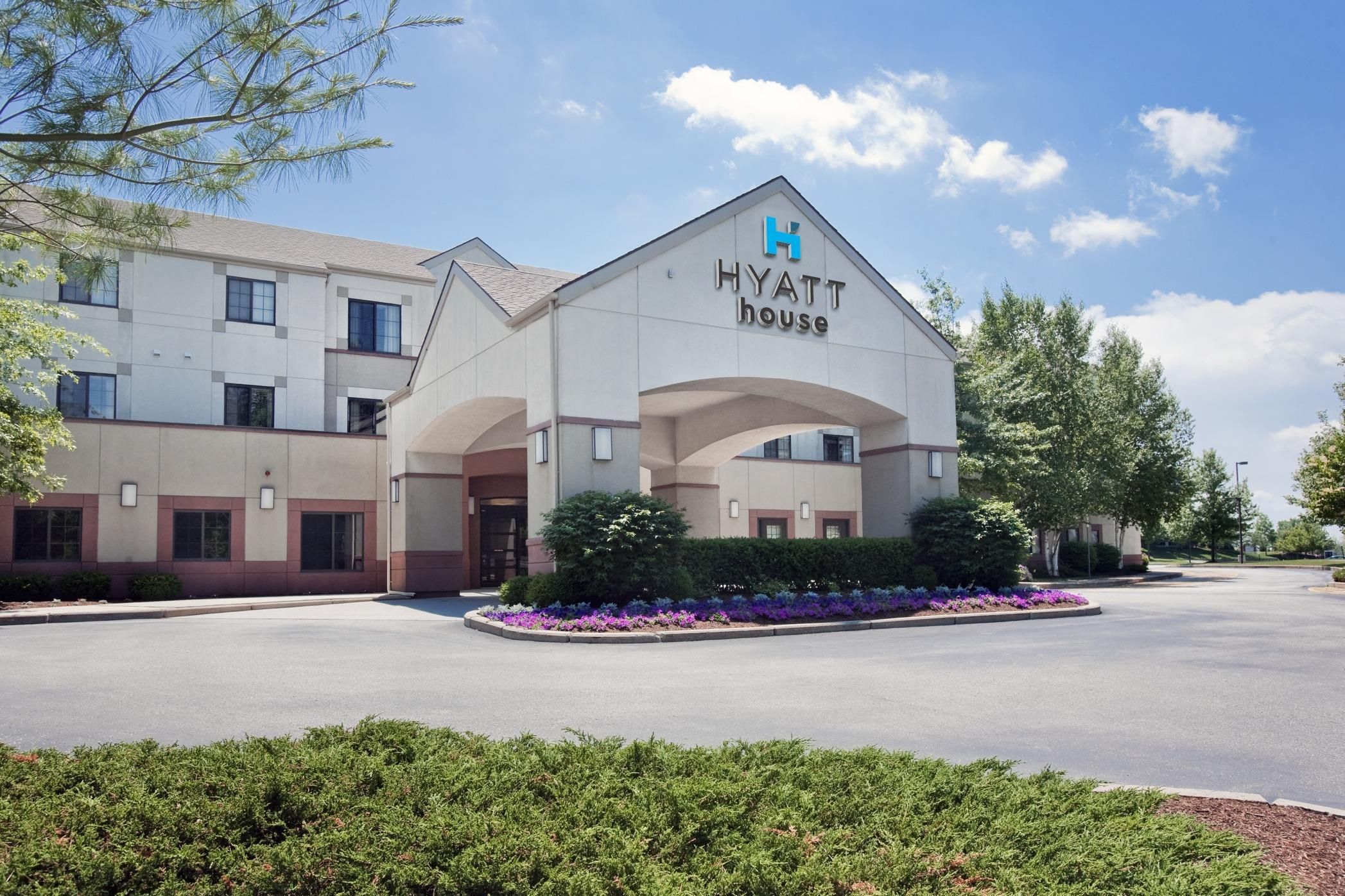 A modern Hyatt hotel with a prominent entrance, landscaped garden, and a clear sky.