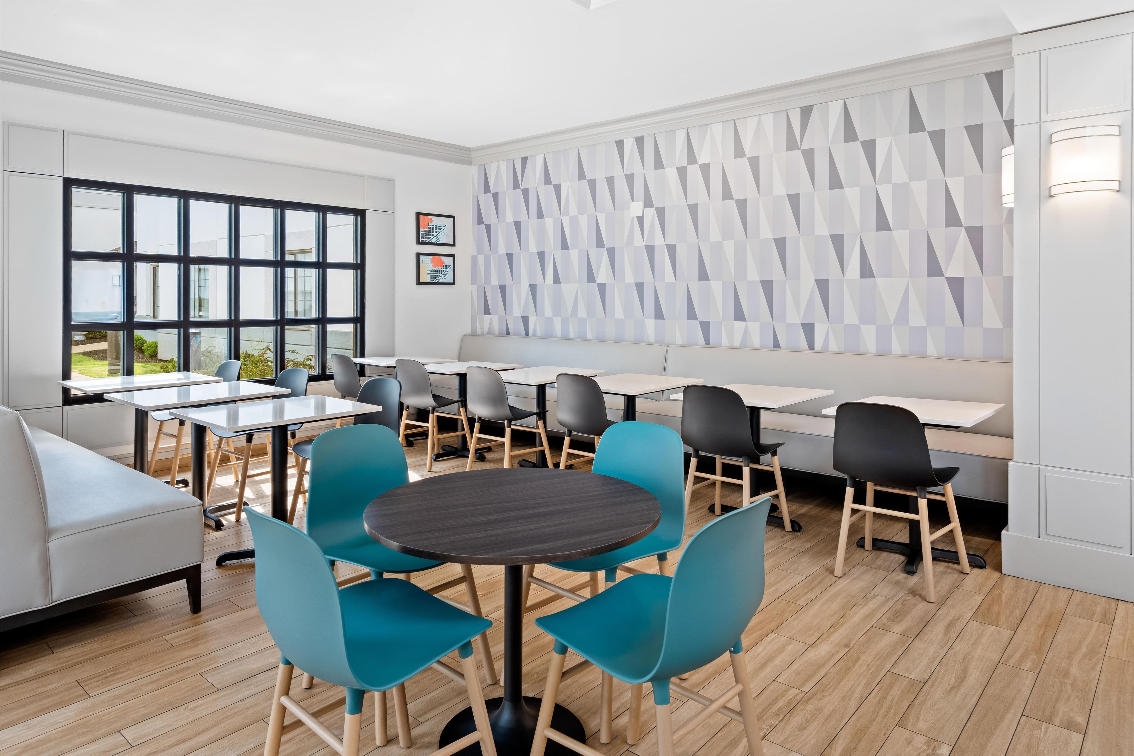 A modern dining area with a mix of round and rectangular tables, blue and black chairs, and a geometric patterned wall.