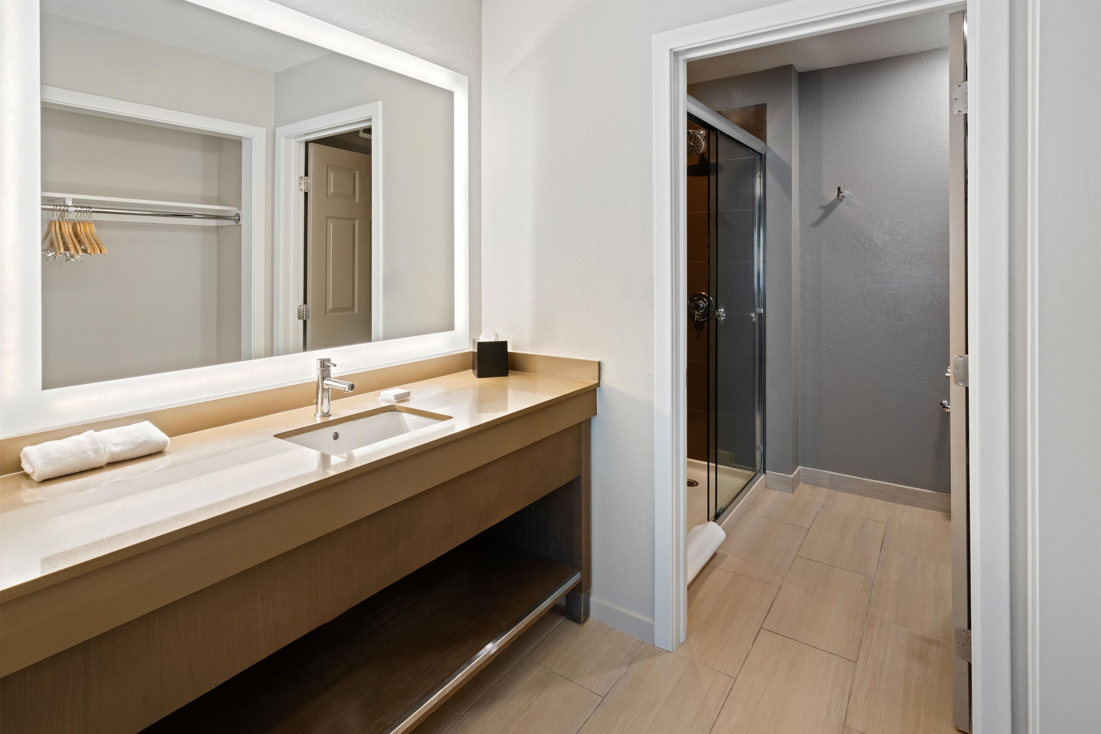 Un baño moderno con un espejo grande, un lavamanos y una ducha.