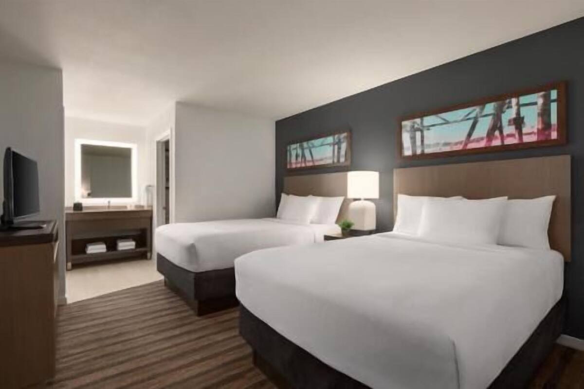 A hotel room with two beds, a TV, a desk, and artwork on the walls.