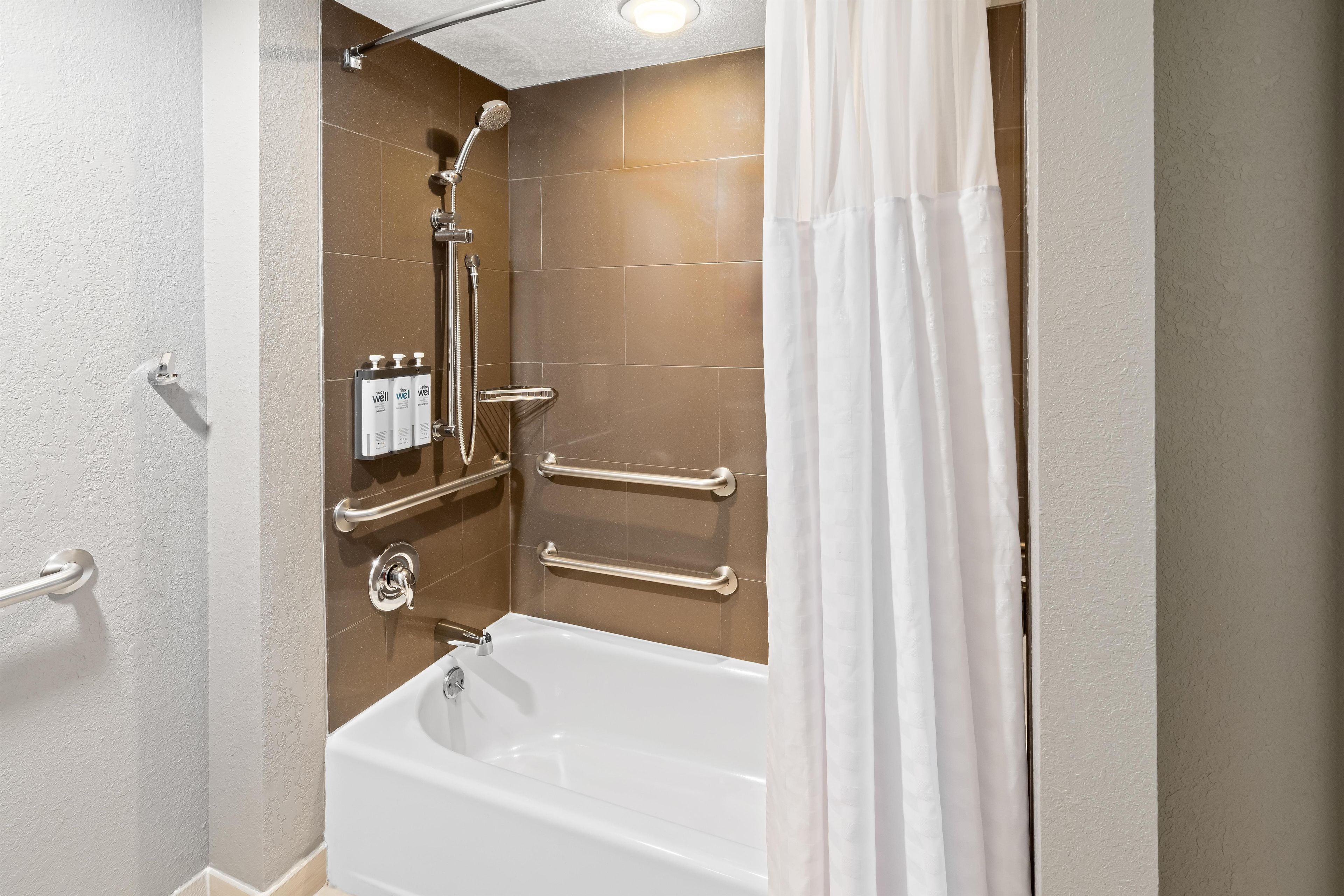 Un baño con bañera, ducha y barras de apoyo.
