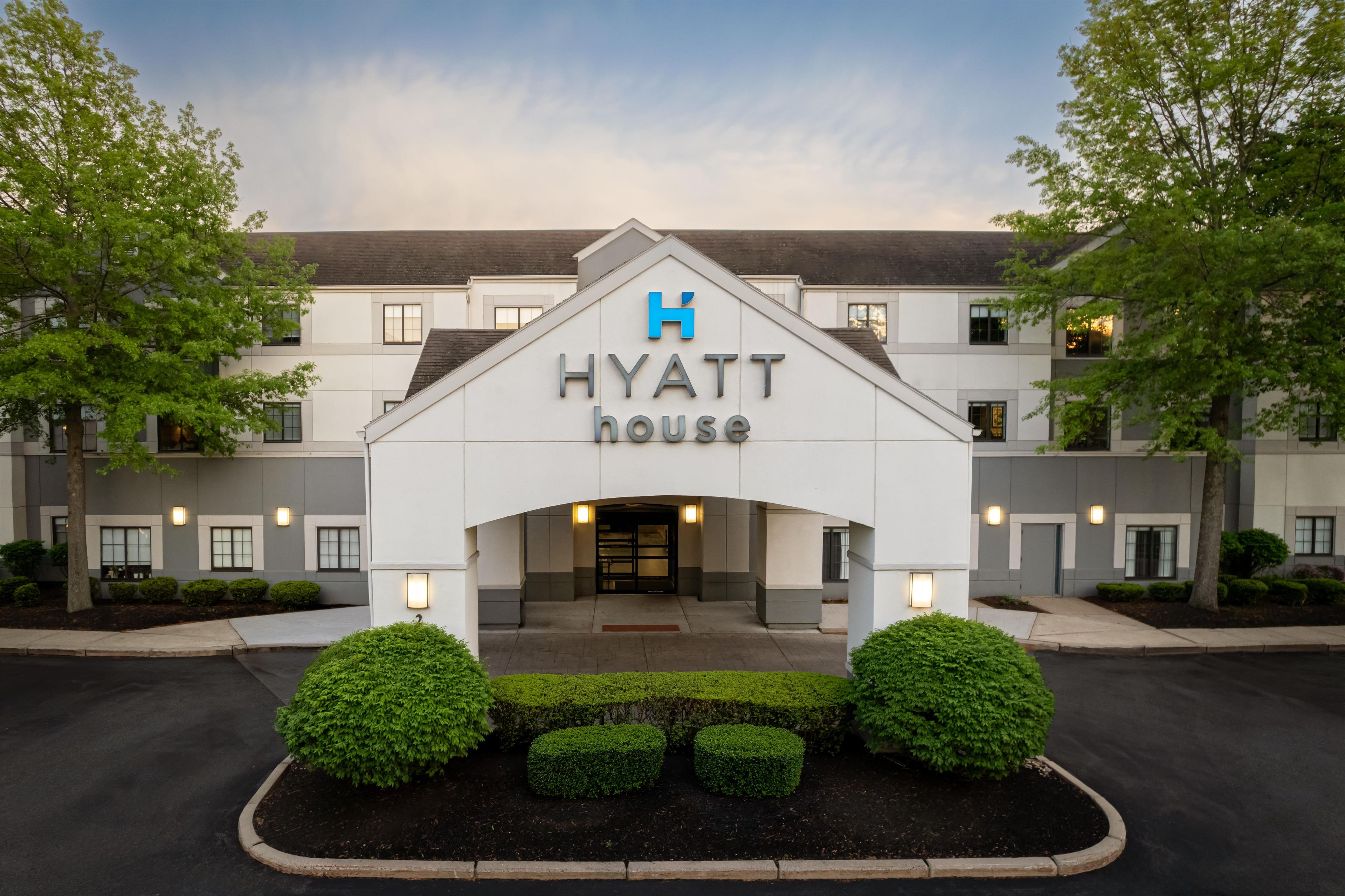 A Hyatt House hotel entrance with a modern design, including a prominent 'H' logo, a gated entrance, and well-maintained landscaping.