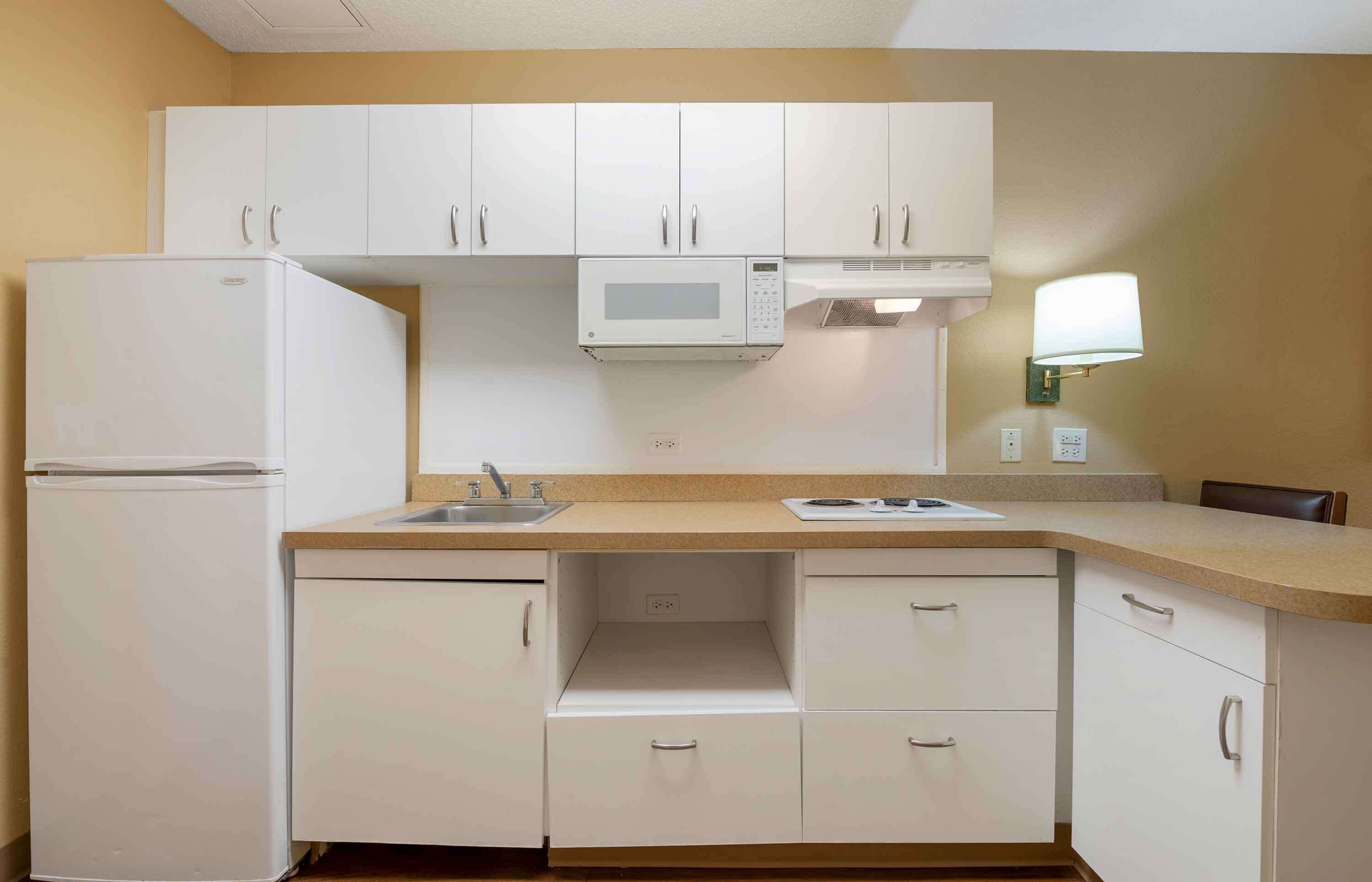 A compact kitchen with white cabinets, a microwave, a refrigerator, and a sink.