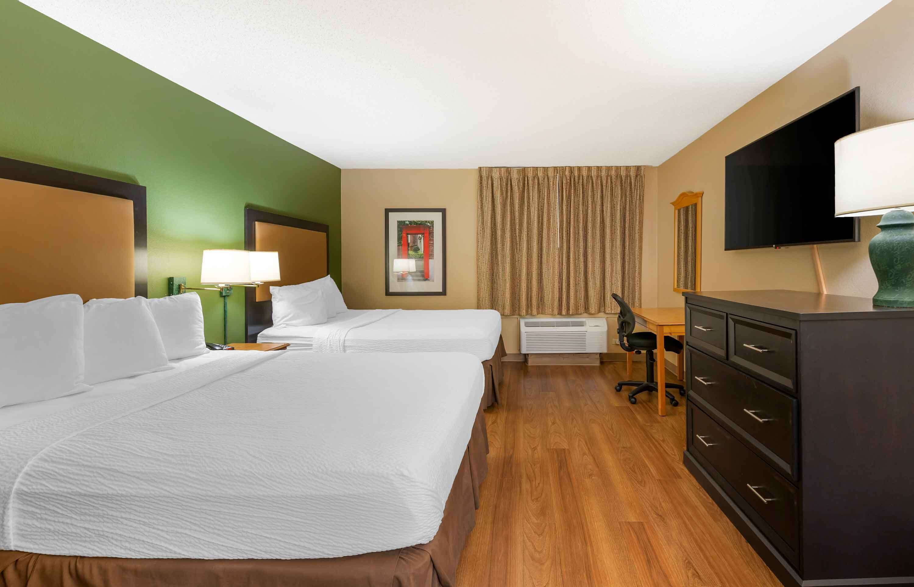 Een hotelkamer met twee bedden, een bureau, een stoel, een televisie en een dressoir.