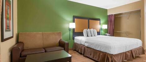 A hotel room with a green accent wall, a brown sofa, a bed with white bedding, and two wall-mounted lamps.