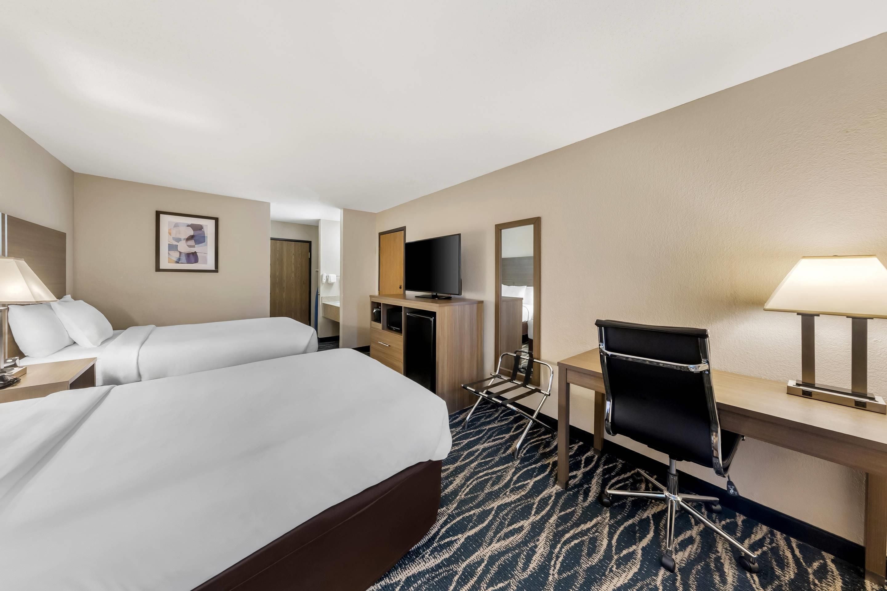 A hotel room with a bed, desk, chair, TV, and a mirror.