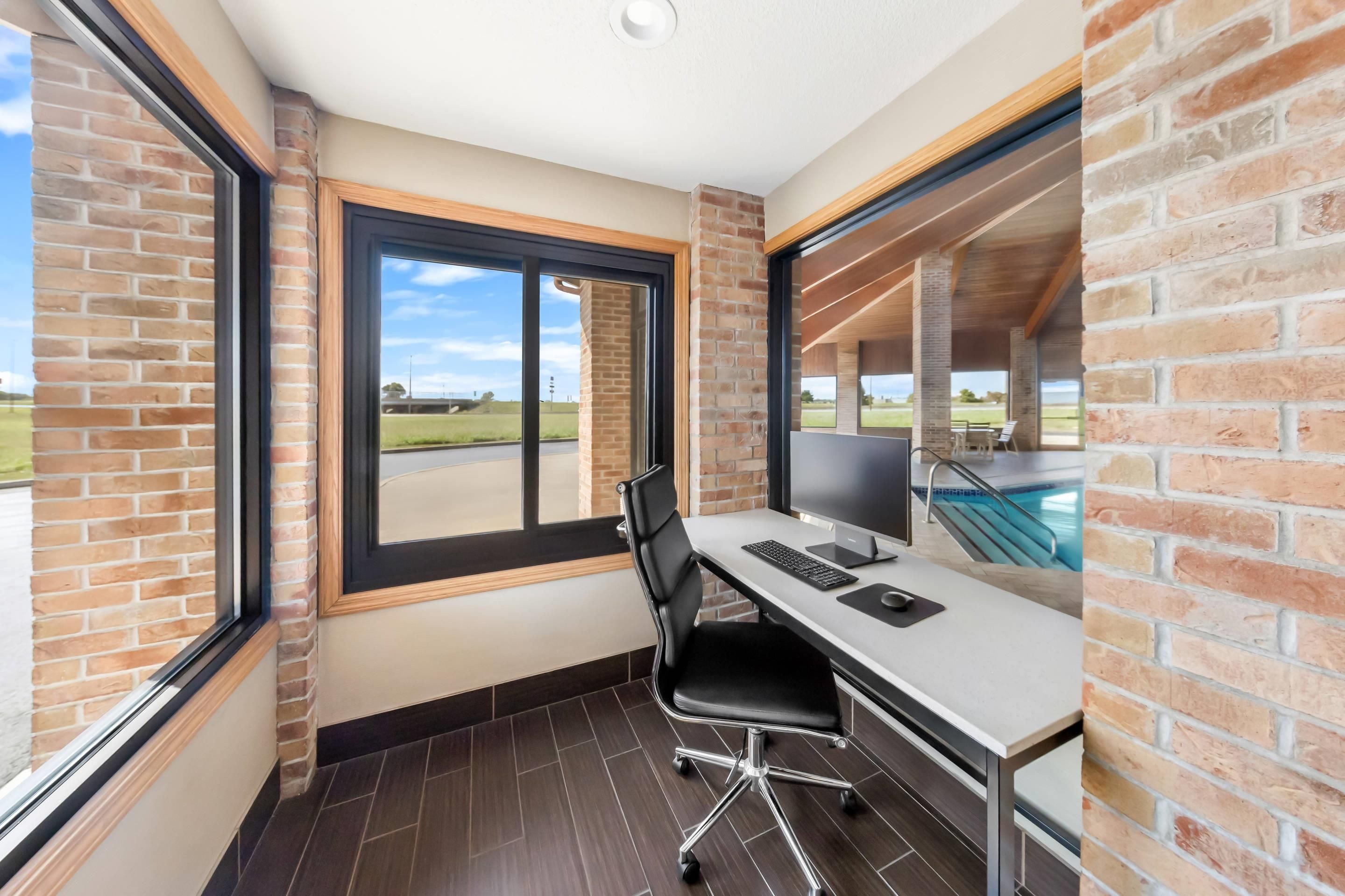 A modern office space with a desk, chair, and computer, large windows, and a view of a swimming pool.