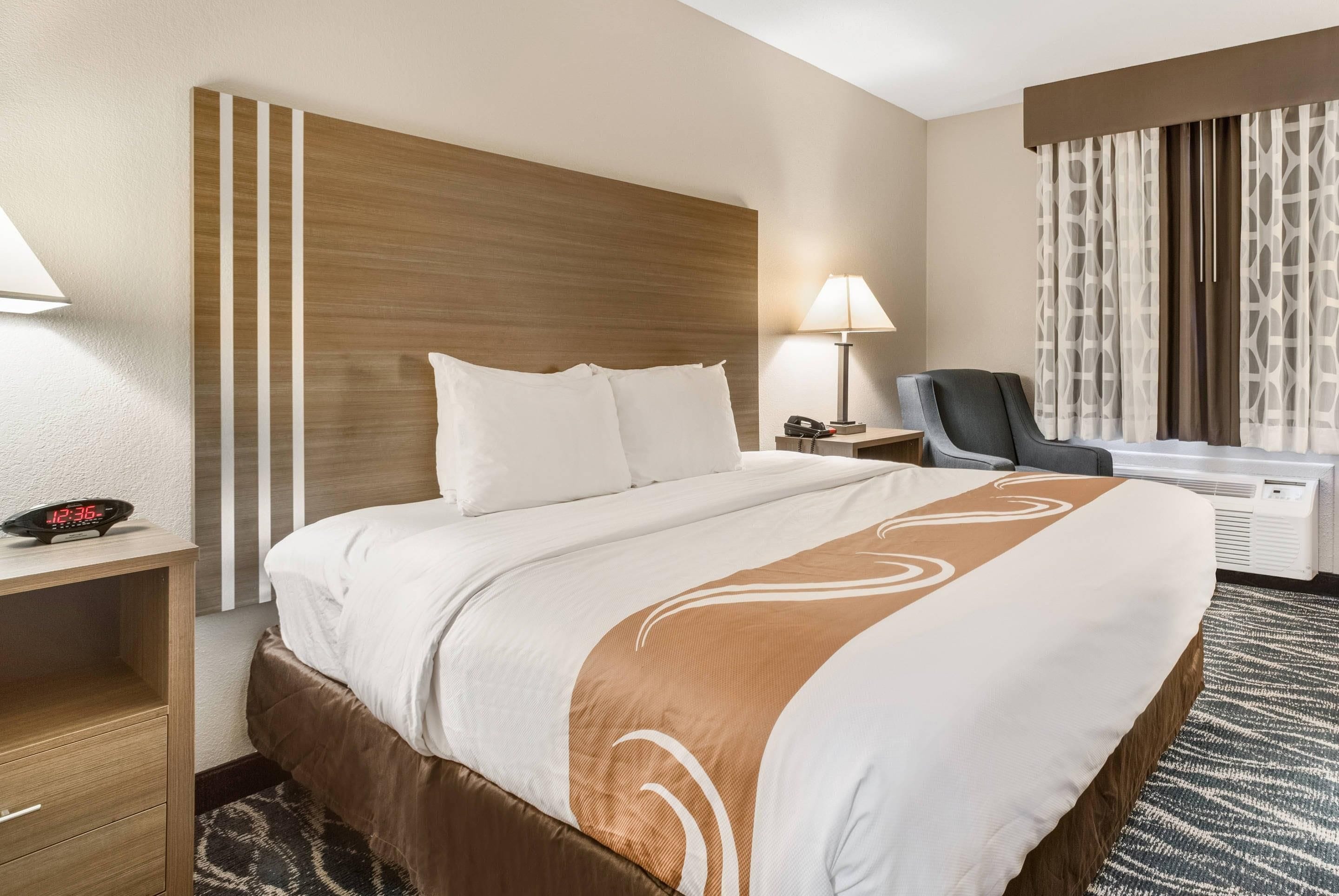 A hotel room with a bed, bedside tables, a chair, a desk, and a lamp.