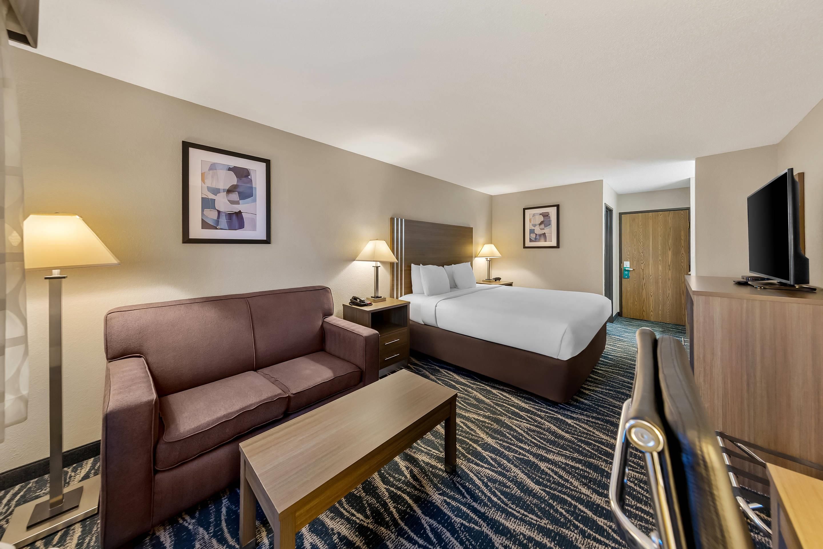 A hotel room with a bed, a sofa, a desk, and a television.