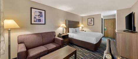 A hotel room with a bed, a sofa, a desk, and a television.