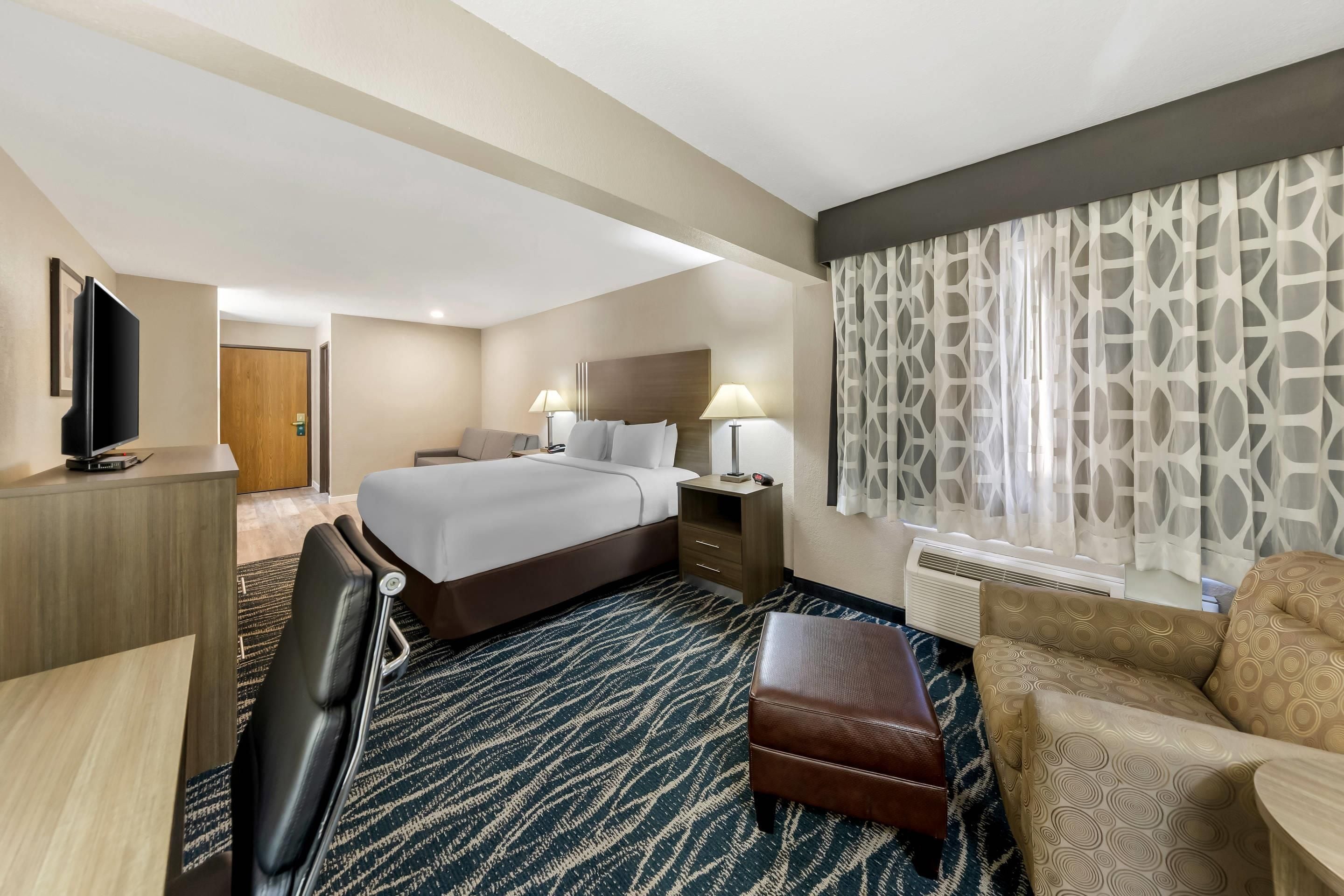 A hotel room with a bed, bedside tables, a desk, a chair, a television, and a window with curtains.