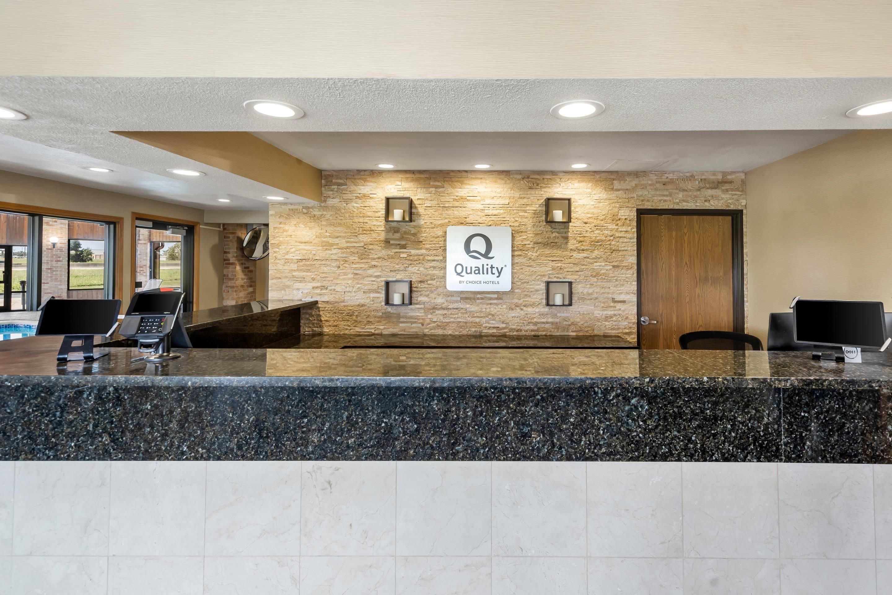 Un hall d’accueil d’hôtel avec un mur en pierre, une enseigne indiquant « Qualité garantie par Choice Hotels » et un comptoir de réception équipé d’ordinateurs.