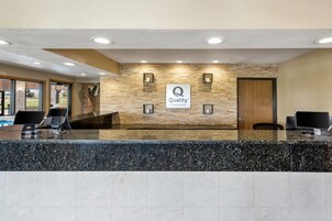 Zona de recepción de un hotel con pared de piedra, un cartel que dice 'Quality by Choice Hotels' y un mostrador de recepción con computadoras.
