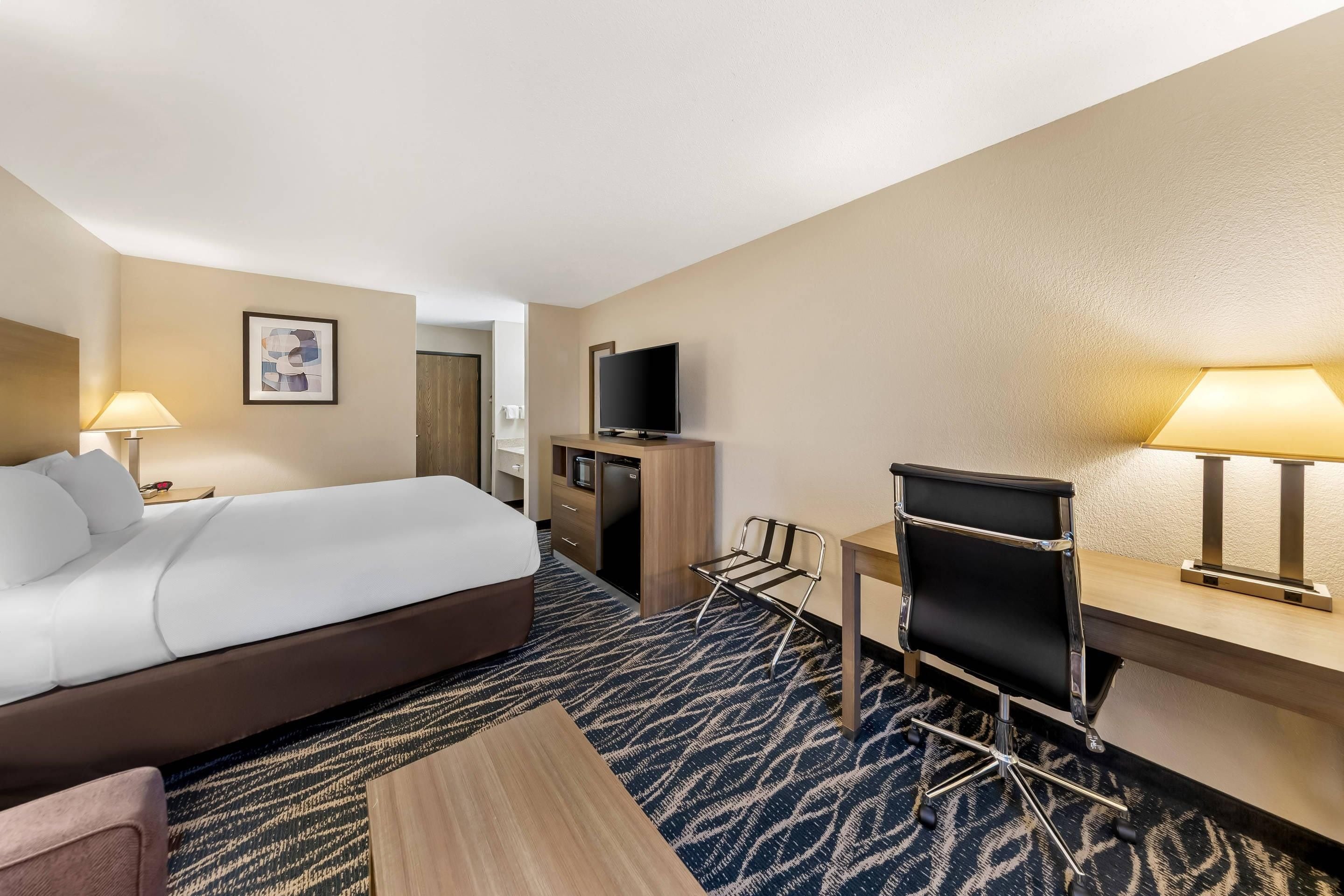 A hotel room with a bed, desk, chair, TV, and a painting on the wall.