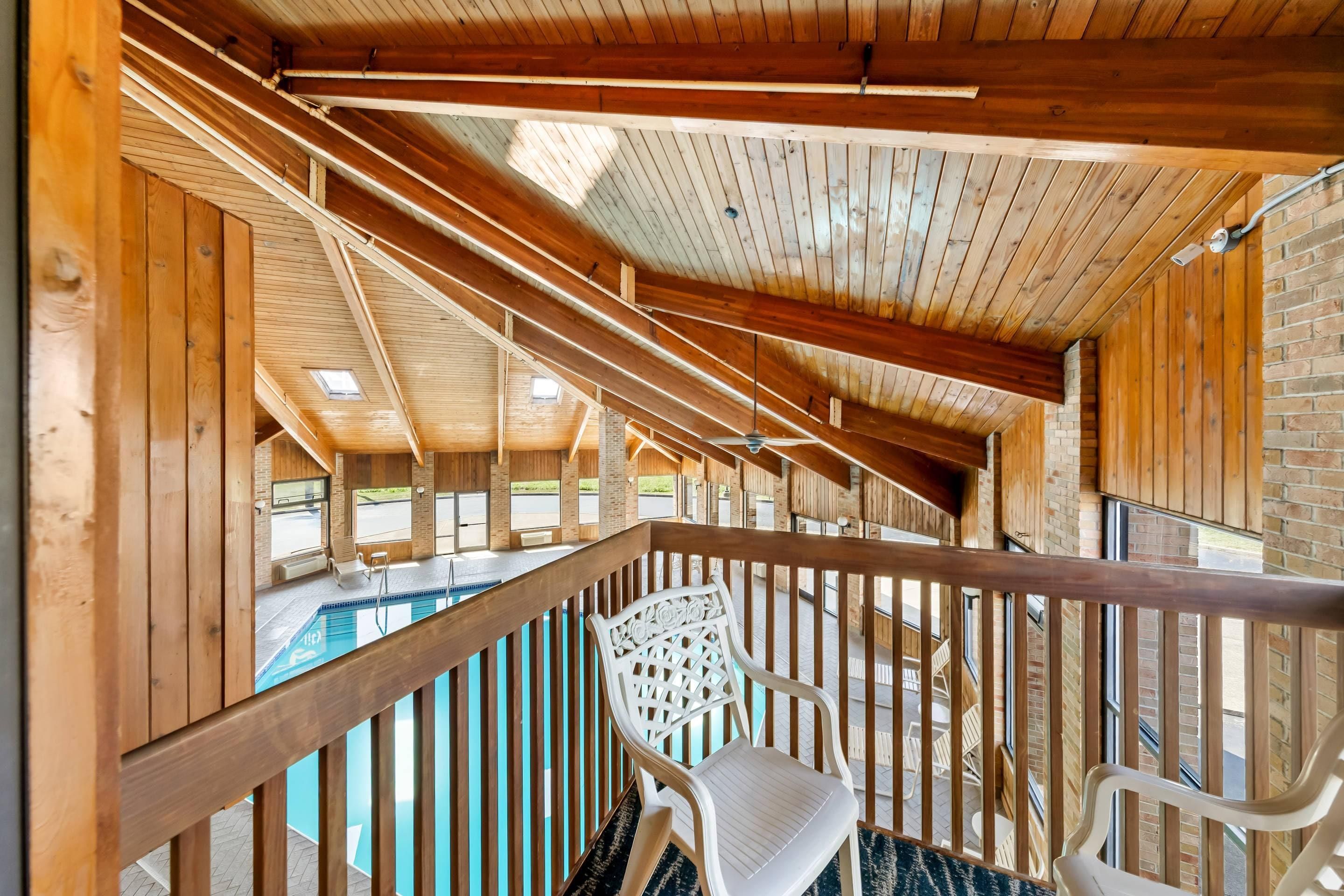 A wooden balcony with a pool, a chair, and a view of the outside.
