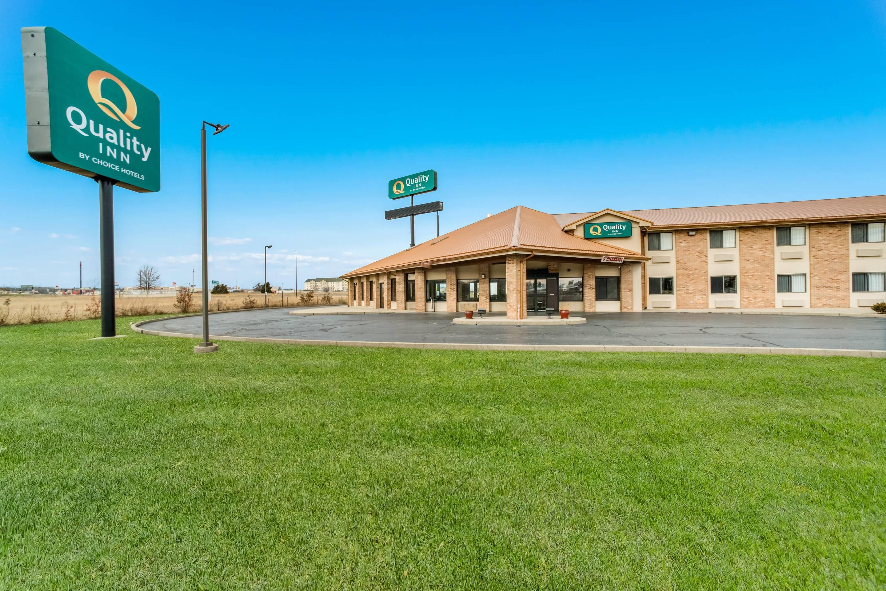 A Quality Inn hotel with a clear sky, a grassy area in front, and a parking lot.