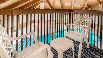A balcony with wooden beams, a pool, and white plastic chairs.
