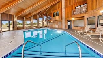 A large indoor swimming pool with clear blue water, surrounded by wooden walls and large windows.